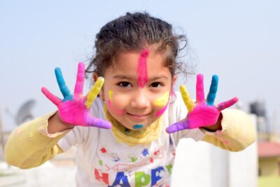 Image of a young girl with colorful paint on her hands and cheeks.