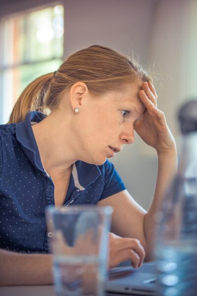 Image of woman aat table with hand on forehead looking stressed.